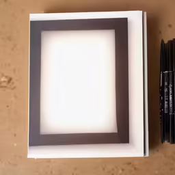 a square white lightbox with black crayons sitting next to it
