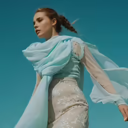 a girl wearing a dress and long scarf against a blue sky