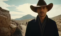 the man wearing the cowboy hat is standing in the middle of a road