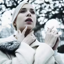 the blonde woman with a white coat is posing