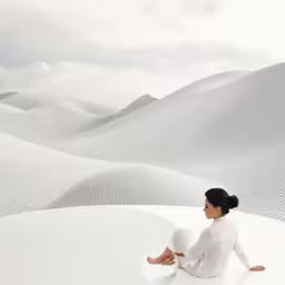 a woman sitting on a white blanket in front of sand dunes