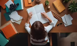 a woman sits at a wooden table and writes on paper