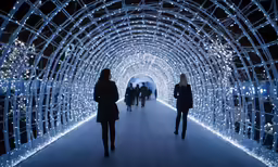 people walking in a tunnel with christmas lights
