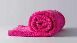 there is a bright pink towel lying on the ground,a folded up towel in front of a gray background