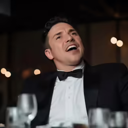 a man dressed in tuxedo looking up and laughing