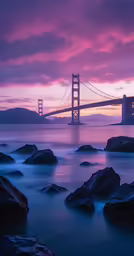 the golden gate bridge at dusk over rocks near a body of water