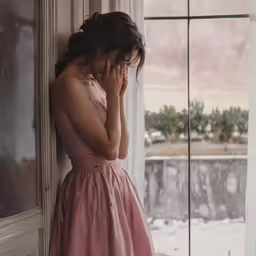 a young woman leaning against a window in a dress