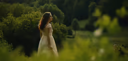 a woman in a white dress walks through tall grass near bushes