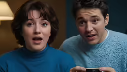 two people holding remotes looking surprised at a camera