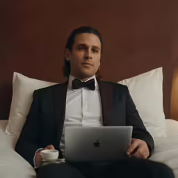 a man in tuxedo using laptop on bed