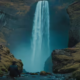 a person sitting on a cliff at the base of a waterfall