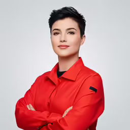 a young woman in a red shirt standing with her arms crossed