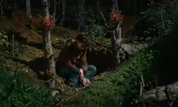 a woman in red hoodie crouching on dirt path next to trees