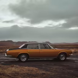 an orange old car parked in a field on a cloudy day
