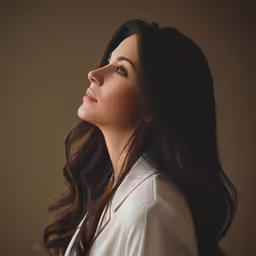 a woman wearing white with long hair and looking upwards at the sky