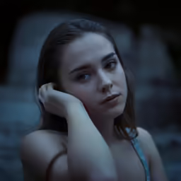 a woman sitting against rocks with her hand on her head
