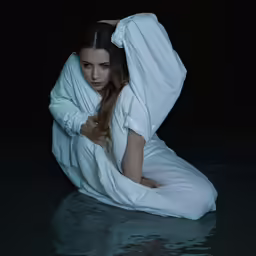 a beautiful young woman sitting on top of a body of water