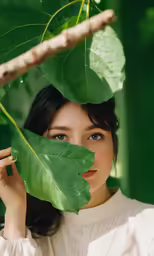 a young woman holding a green leaf with a serious look on her face