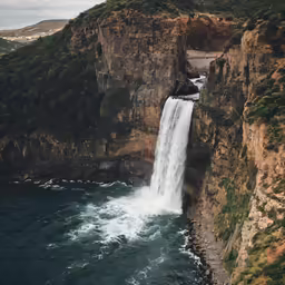 an aerial view of a waterfall with several rocks, and a bridge