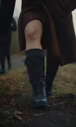 a woman in boots and brown coat is walking