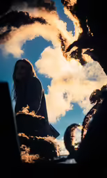 a person sitting against a sculpture and some clouds