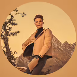 a woman is wearing a coat and smiling in front of mountains