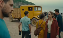 people stand and stare at an old yellow truck on the beach