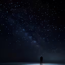 a dark sky and a lone man looking at the stars