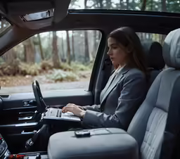 a woman sitting in the drivers seat of a car using a laptop