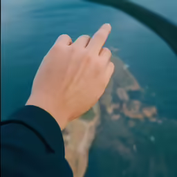 a hand pointing towards the water below in an airplane