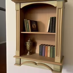 an old wooden shelf with books on top of it,an antique shelf with a cup on it,a corner of a shelf containing books and a book case,a wall shelf holding books and vase,a book shelf with two books and a golden cup