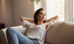 a beautiful woman sitting on a white couch next to a potted plant
