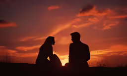 two people sitting against the sunset with their hands in their pockets