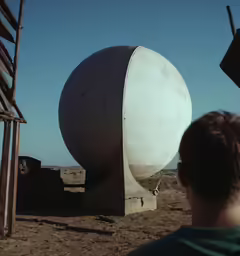 a man standing in a desert looking at a big object