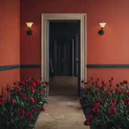 a group of red flowers grow in the ground by a door