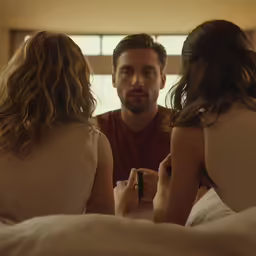a man sits in bed next to two young women