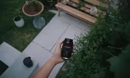 a hand holding a camera near a park bench