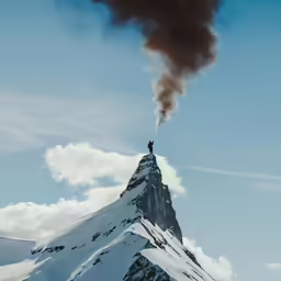 the lone person is standing on the top of a tall mountain as black smoke comes out of the chimney