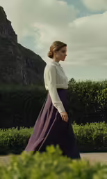 a woman wearing a purple dress in front of hedges