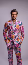 a man standing wearing a pink floral suit with his hands on his hips,a man with a pink suit and tie standing