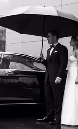 a bride and groom stand under an umbrella beside a car