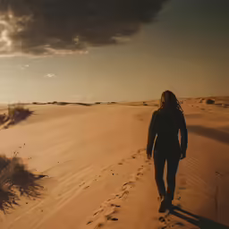 a woman walking down a desert path toward a sunset