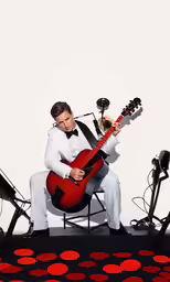 man in tuxedo sitting on a stage playing the guitar
