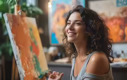a woman smiles while sitting in front of a easel