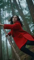 a woman wearing a red coat climbing on a tree branch