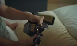 person holding up a digital camera on a bed