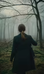 a woman walks through the woods with trees in fog