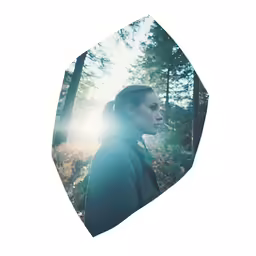 a woman stands in a forest looking up at the sun
