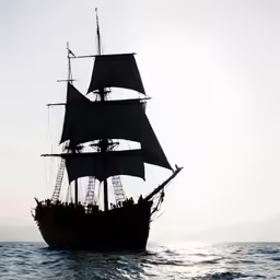 a sail boat sailing in the ocean near a mountain range