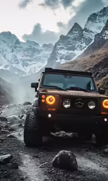 a brown jeep is driving on rocky terrain near snow covered mountains